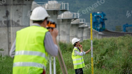 Preview: Two Construction workers are standing in a field, one of them holding a yellow tape measure