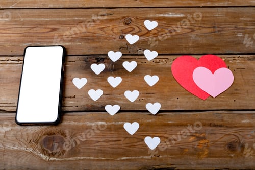 Preview: Overhead view of smart phone by heart shaped decoration on wooden table, copy space
