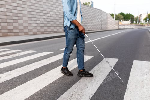 Preview: Unrecognizable young black visually impaired man with cane walking across city street, closeup