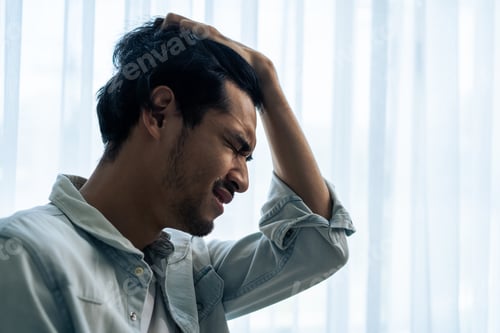 Preview: Asian young upset depressed man sitting alone in living room at home.