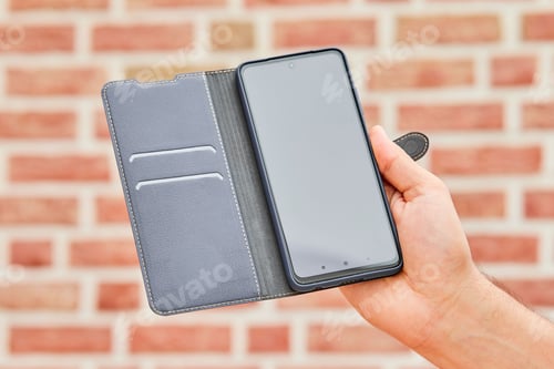 Preview: Smart phone with a leather case in a girls hand with a brick wall on the horizon