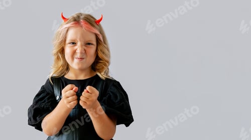 Preview: Little girl wearing red horns and black dress with clenched fists on gray background.
