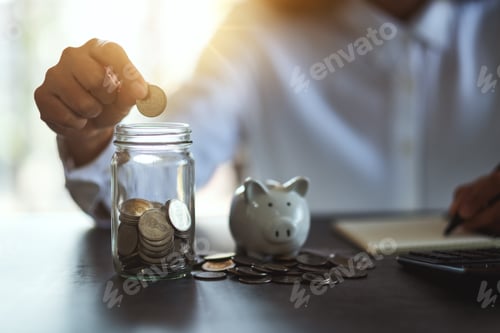 Preview: a woman putting coins in a glass jar and taking note with piggy bank on the table