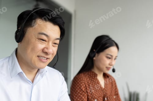 Preview: Asian business professionals in a modern office environment wearing headsets engaged in customer