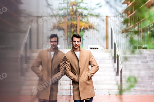 Preview: Portrait of stylish handsome young man with coat standing outdoors and leaning on wall.
