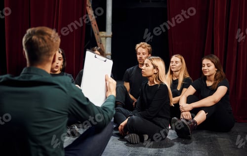 Preview: Sitting on the floor. Group of actors in dark colored clothes on rehearsal in the theater
