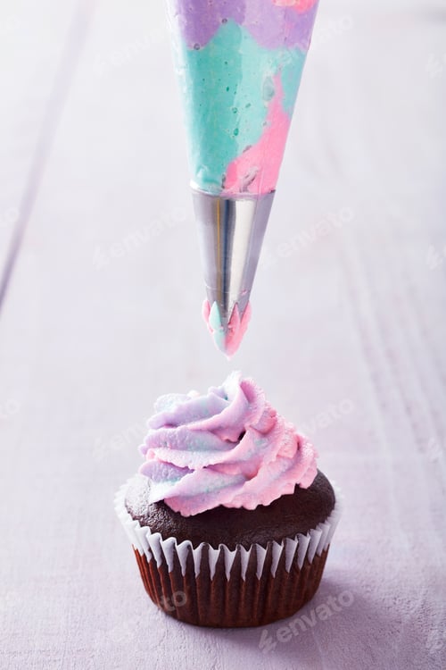 Preview: Chocolate cupcake with pink, purple, and blue icing being piped on top.