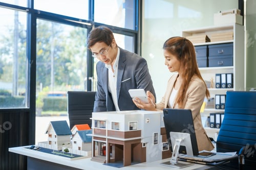 Aperçu: A businessman and woman sit at a table, discussing a two-story house for sale in a village project