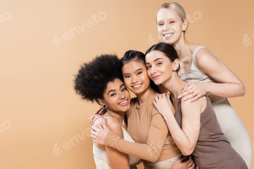 Preview: pleased multiethnic models embracing and smiling at camera while posing in lingerie isolated on