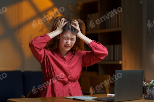 Preview: Stressed Asian Freelancer Woman Holding Head in Hands at Home Office Desk