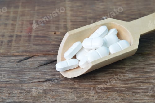 Preview: White Pills in a Wooden Scoop on Wood Surface