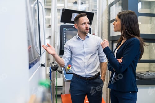 Preview: Businessman and businesswoman talking at a machine in modern factory
