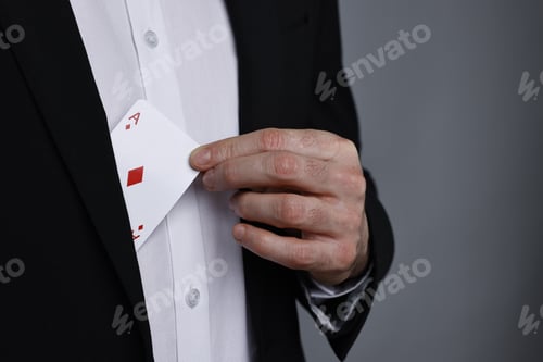 Preview: Illusionist hiding playing card behind jacket lapel on grey background, closeup