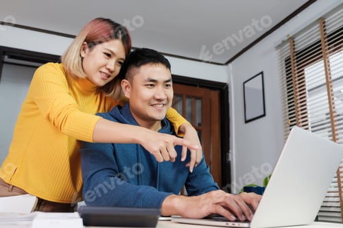 Preview: Asian couple watching video live straming on laptop at table