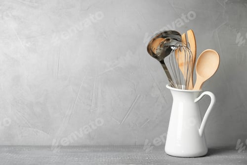 Preview: Jug with kitchen utensils on wooden table against light grey background. Space for text