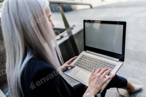 Vista previa: Joven empresaria sentada en las escaleras de la ciudad con el ordenador portátil