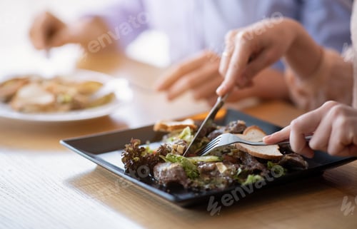 Preview: Cropped view of millennial couple eating tasty meat and vegetable salad at table in cafe