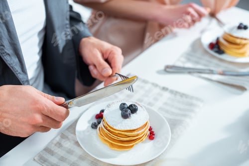 Preview: cropped view of woman and man having pancakes during breakfast in kitchen