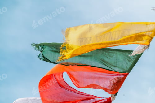 Preview: Colorful torn fabric flags fluttering in wind against clear blue sky