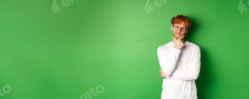Preview: Intrigued young man with red hair, wearing glasses, looking at camera pleased and thoughtful