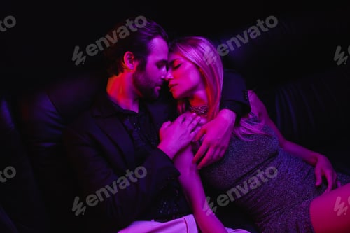 Preview: Side view of sexy couple kissing on leather couch with lighting during party isolated on black