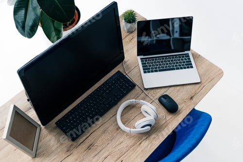 Preview: high angle view of table with laptop with blank screen, computer, headphones, potted plant, photo
