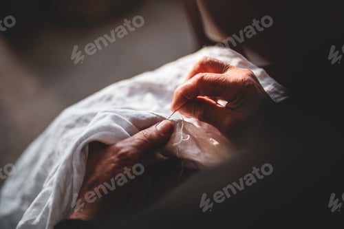 Preview: Female holds a needle in her hands and embroiders a pattern with white threads on a white cloth