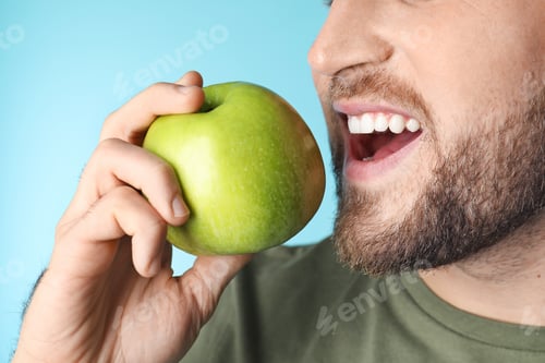 Preview: Young man with healthy teeth and apple on color background, closeup