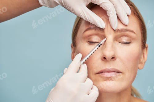 Preview: Cosmetologist giving injection in the glabellar wrinkle for mature woman