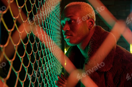 Preview: Young African man in furcoat standing close to bars