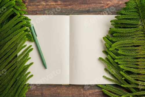 Preview: top view open book with green pen and pine leaf on wooden table background