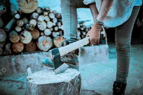 Preview: A woman sticks an axe in a log. She wears gloves and mountain boots.