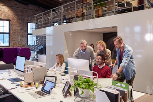 Preview: Colleagues looking over shoulder of young man working in modern office