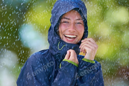 Preview: Cropped shot of a young woman standing happily in the rain with her raincoat