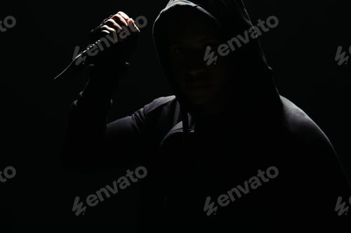 Preview: Silhouette of hooligan in hoodie holding knife isolated on black with lighting