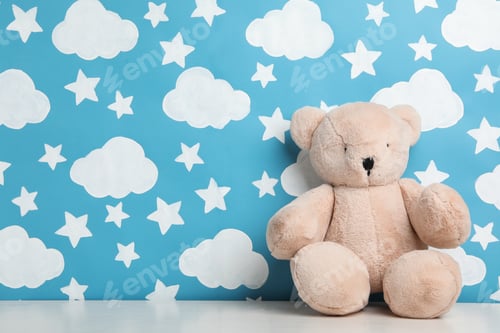 Preview: Teddy bear on white wooden table near wall with painted blue sky, space for text. Baby room interior