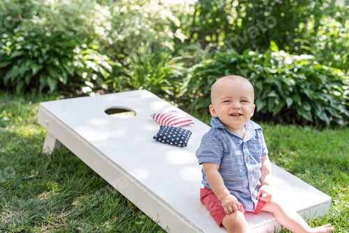 Preview: Portrait of little boy sitting on cornhole game board in backyard in summer