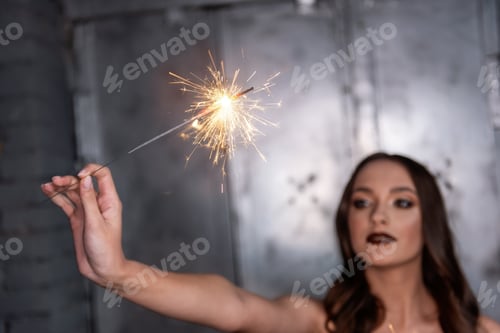 Preview: Blurred Beautiful girl, holds bright sparklers in focus in hands.
