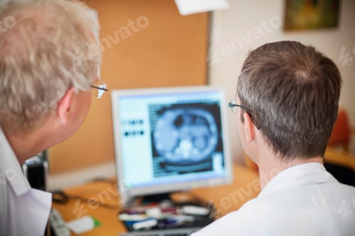 Preview: Rear view of doctors looking at radiogram image on desktop pc in hospital