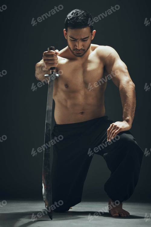 Preview: Full length shot of a handsome young man kneeling in the studio and posing with a broadsword