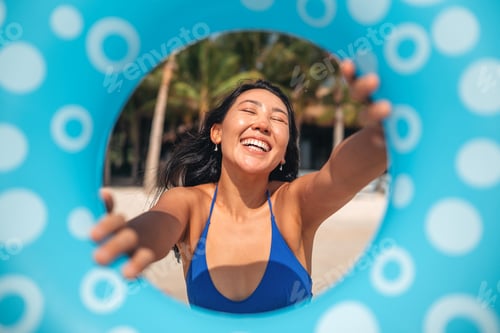 Preview: Cheerful woman posing with a blue swim ring on a sunny tropical beach
