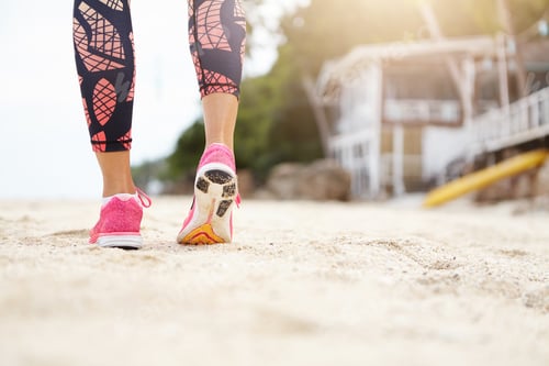 Preview: Cropped shot of female jogger on beach. Caucasian athlete girl in colorful leggings and pink running