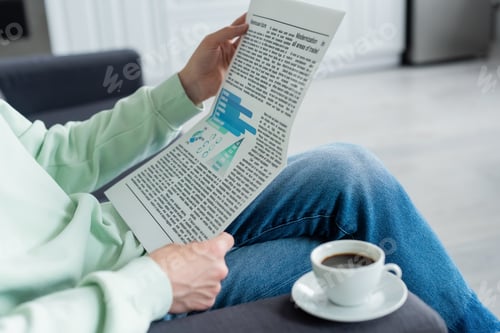Preview: cropped view of man reading newspaper near coffee cup on sofa