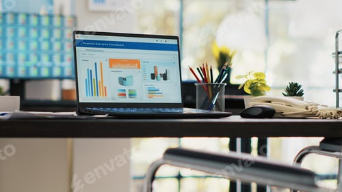 Preview: Wheelchair in inclusive office for employees and laptop on desk showing financial charts