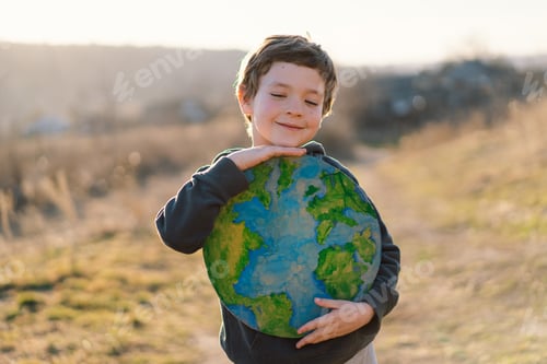 Preview: Little boy holding planet in hands against green spring background. Earth day