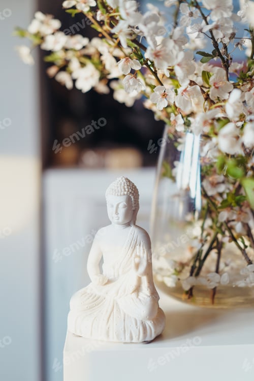Preview: Decorative white Buddha statuette with blooing tree branches in the vase on background. Meditation