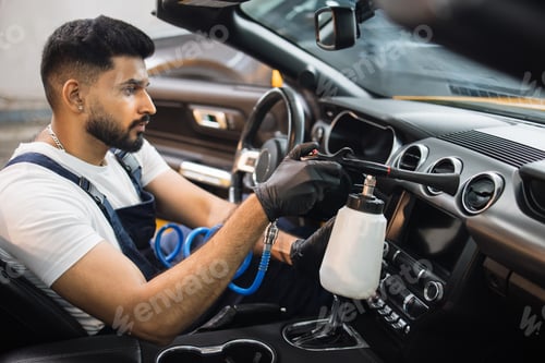 Preview: Male bearded worker of auto service station, cleaning modern vehicle interior with tornado air gun.