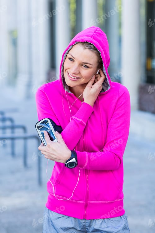 Preview: A woman wearing a pink jacket putting her headphones on a sunny day