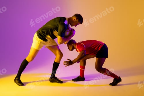 Preview: Diverse male rugby players with rugby ball playing over pink lighting