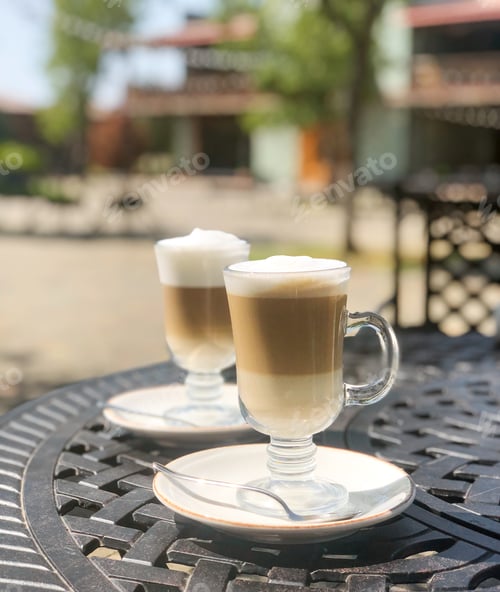 Preview: Coffee latte or cappuccino with milk foam in a tall glasses on a wrought iron table in a street cafe